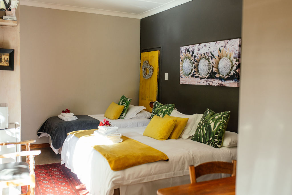 Bedroom with two beds, yellow cushions and a protea artwork