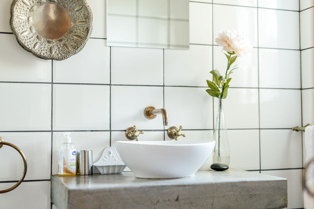 Bathroom basin with brass taps, white tiles and a flower
